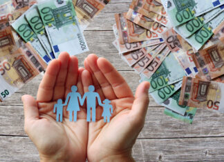 Papierfamilie in der Hand mit Geldscheinen im Hintergrund.