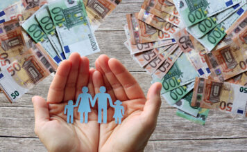 Papierfamilie in der Hand mit Geldscheinen im Hintergrund.