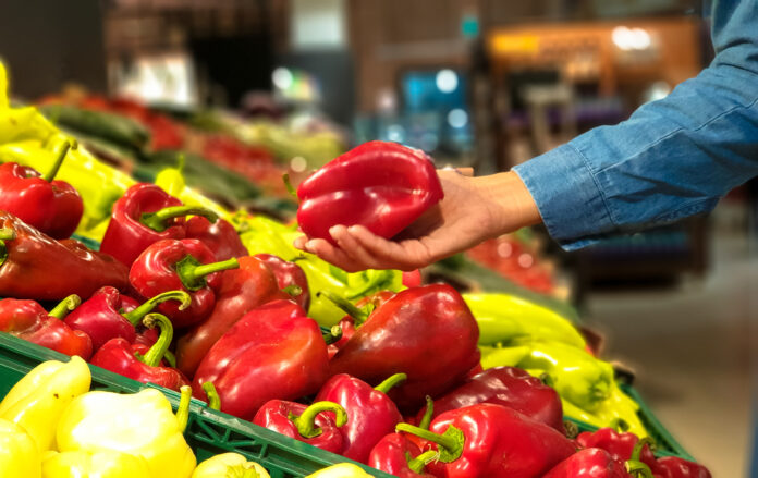 Eine Hand nimmt eine Paprika aus einem Gemüsestand.