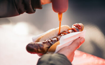 Ketchup wird auf einen Hotdog gegeben.