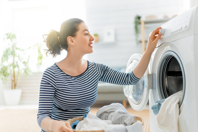 Frau lädt Kleidung in die Waschmaschine, um diese zu waschen