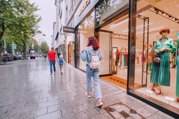 Kunden schlendern über einen Fußweg entlang verschiedene Einkaufsläden