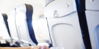 Ein Glas Wasser steht auf einem Tisch in einem Flugzeug. Ein Passagier oder Fluggast greift nach diesem Wasserglas, um zu trinken auf dem Flug.