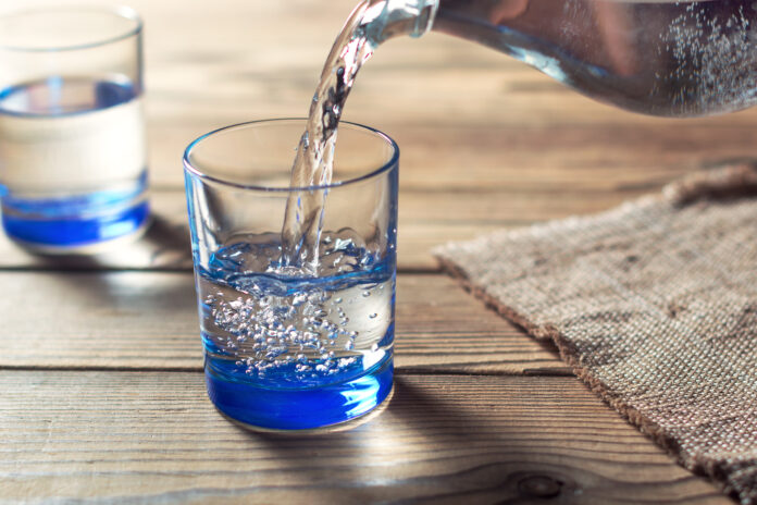 Wasser wird aus einer Karaffe in ein Glas gegossen.