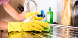 Eine Frau putzt die Oberfläche der Spüle mit einem Schwamm und einem Reiniger