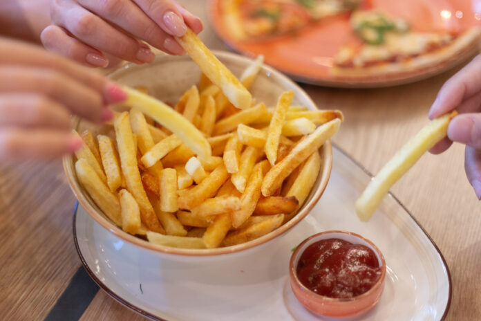 Drei Hände greifen nach frittierten Pommes Frites auf einem Teller mit Ketchup
