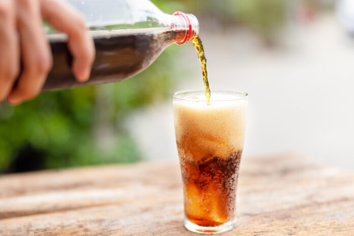 Cola wird aus einer Flasche in ein Glas gegossen.