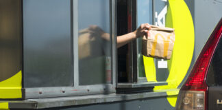 Mann reicht eine McDonalds Tüte an einen Autofahrer im Drive-In.