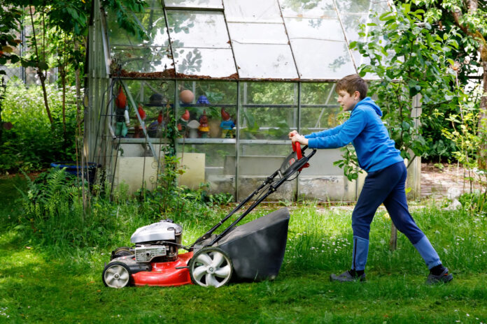 Ein Junge mäht Rasen und macht Gartenarbeit.