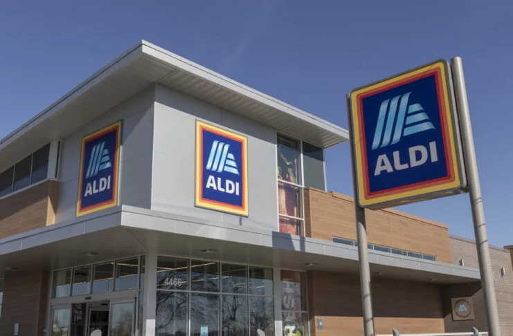 Aldi Discounter Filiale Außenansicht Supermarkt Einkaufen Lebensmittel Geschäft Eine moderne Filiale des Supermarkts Aldi ist vor dem blauen Himmel zu sehen. Oben auf dem Gebäude und auf einem Schild ist jeweils das Aldi-Logo abgebildet.