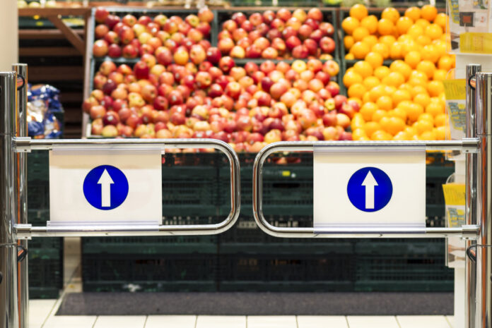 Der Eingang eines Supermarktes, im Hintergrund Äpfel und Orangen