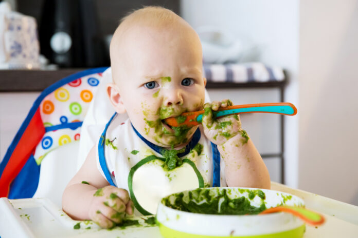 Ein Baby isst in einem Hochstuhl gesunden Spinat