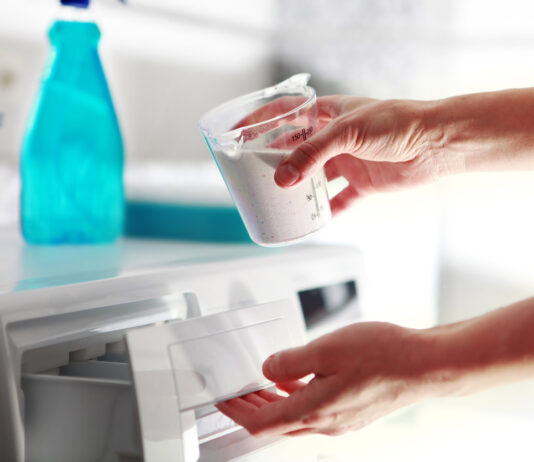 Eine Hand füllt Waschmittel in die Waschmaschine