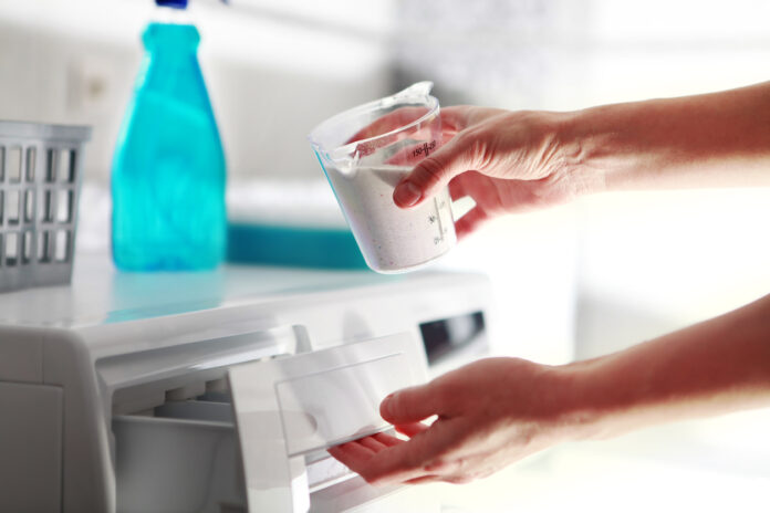 Eine Hand füllt Waschmittel in die Waschmaschine