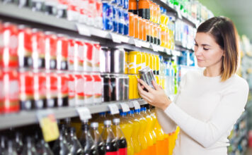 Eine Frau steht im Supermarkt und hält ein Getränk in der Hand
