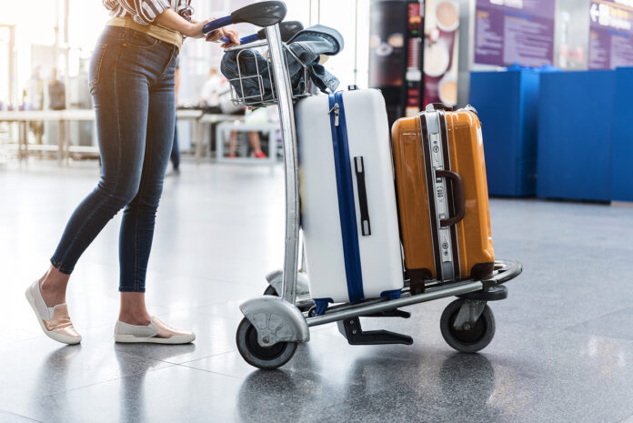 Frau rollt ihre Koffer auf einem Flughafen.
