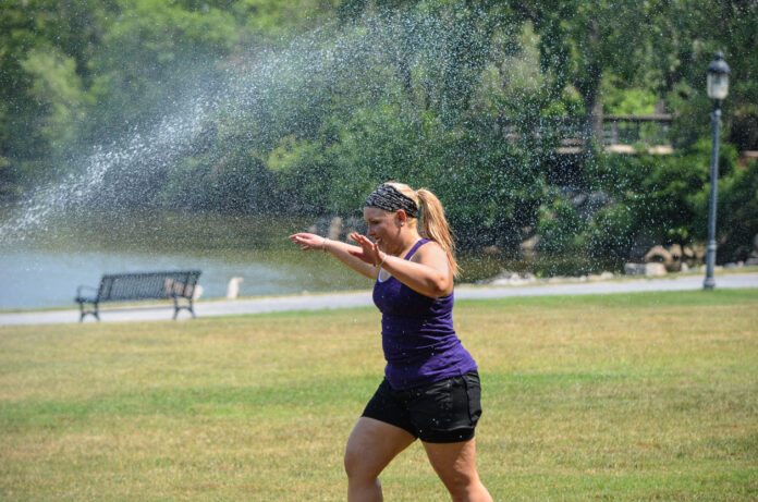 Eine Frau läuft durch einen Sprenger im Park.