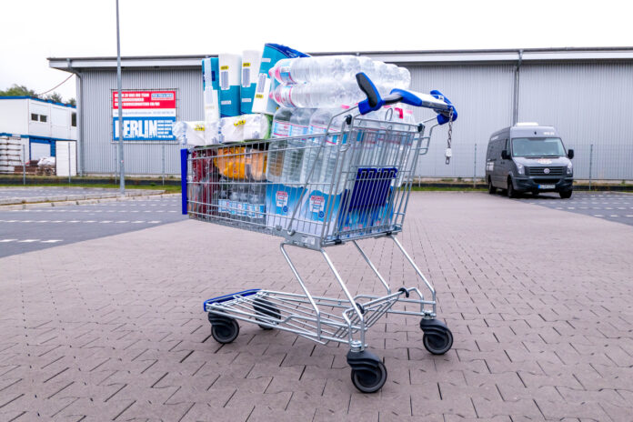Ein übervoller Einkaufskorb mit Lebensmitteln und Getränken vor einem Supermarkt auf dem Parkplatz