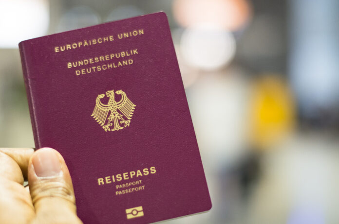 Ein Mann hält einen Reisepass der Bundesrepublik Deutschland, der Europäischen Union, in die Höhe. Der Pass ist gestochen scharf, während der Hintergrund verschwommen und nicht erkennbar ist.