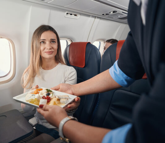 Reisen mit dem Flugzeug. Eine Frau erhält ihr Essen von der Stewardess.