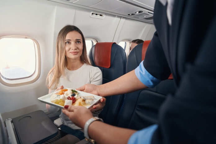Reisen mit dem Flugzeug. Eine Frau erhält ihr Essen von der Stewardess.