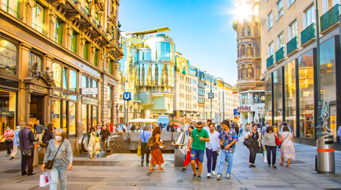 Passanten laufen durch eine Altstadt an Laden Filialen vorbei und gehen einkaufen