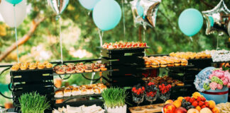 Ein Tisch mit einer Vielzahl von Snacks und Scheiben. Essen auf einer Open-Air-Party. Mini-Burger und Kanapees. Dekorierter Tisch mit Essensblumen und Gras.