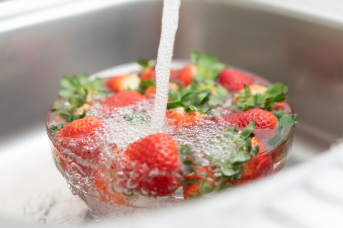 Erdbeeren in einer Spüle unter fließendem Wasser waschen, damit sie so richtig süß schmecken