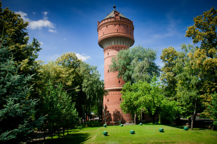 Ein Wasserturm inmitten einer Parkanlage mit großen Laubbäumen