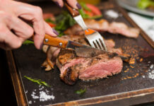 Eine Frau hält ein Messer und eine Gabel beim schneiden von einem Steak