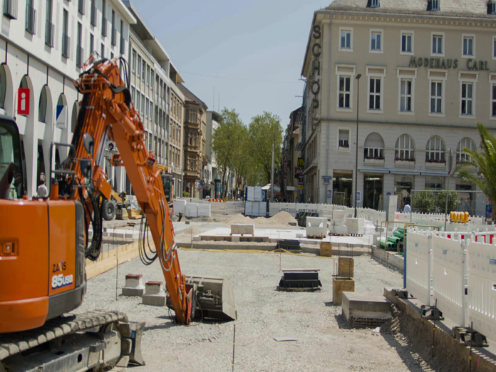 Arbeiten mit Baustelle in der Innenstadt. Ein Kran baggert den Boden auf, außerdem werden Steine verlegt. Es kommt zu einer Vollsperrung auf dem Marktplatz durch die Bauarbeiten.