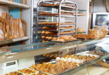 In einer Bäckerei liegen verschiedene Backwaren in der Auslage. Auf einem mobilen Wagen und im Hintergrund sind zudem viele Baguettes zu sehen.