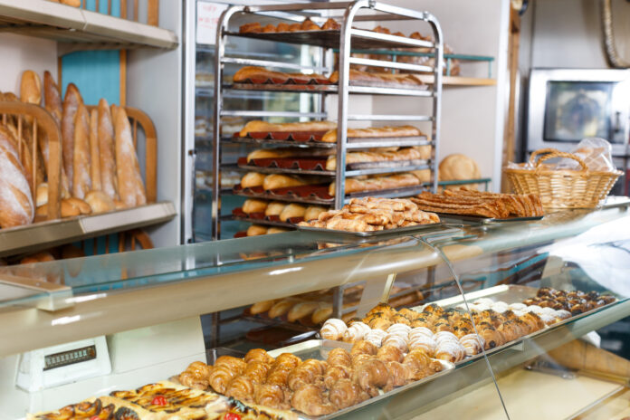 In einer Bäckerei liegen verschiedene Backwaren in der Auslage. Auf einem mobilen Wagen und im Hintergrund sind zudem viele frische Baguettes zu sehen, die für Kunden bereitliegen.