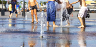 Kinder spielen am Wasser, das aus Fontänen aus dem Boden auf einem Platz in der Stadt kommt.