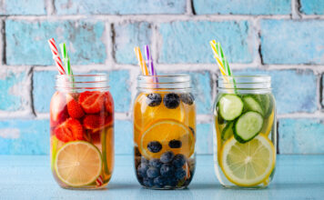 Mehrere Trinkgläser mit verschiedenen Obst- und Gemüsestücken in Wasser mit einem Trinkhalm