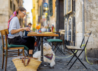 Frau isst italienische Pasta, während sie mit einem Hund im Restaurant auf der Straße in Rom sitzt.
