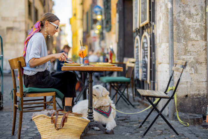 Frau isst italienische Pasta, während sie mit einem Hund im Restaurant auf der Straße in Rom sitzt.