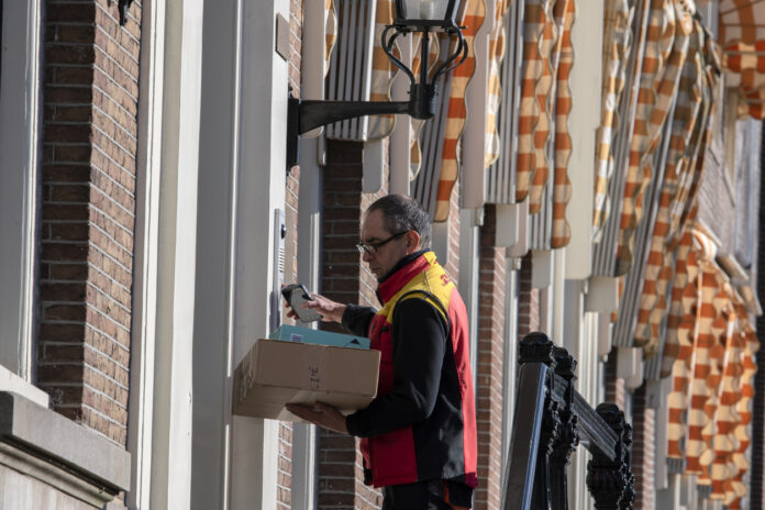Ein DHL-Bote klingelt an Haustür mit Paket in der Hand