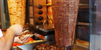 Ein Mitarbeiter in einem Döner-Imbiss schneidet Fleisch von einem Dönerspieß ab