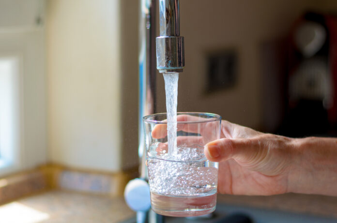Eine Frau füllt ein Glas mit Leitungswasser aus einem Wasserhahn.