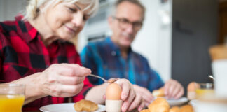 Zwei ältere Menschen sitzen beim Frühstück und die Frau isst ein Frühstücksei