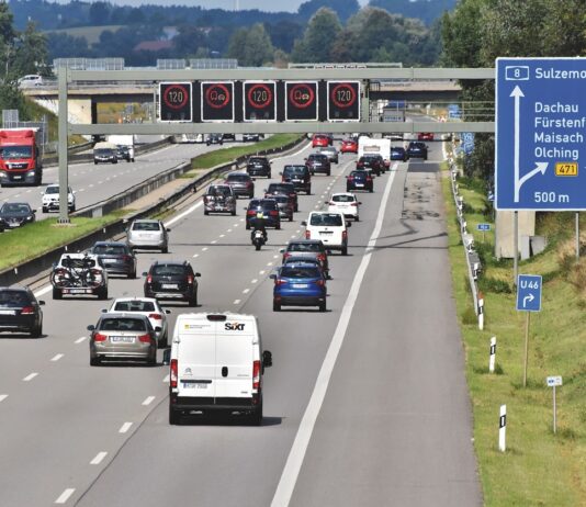 Roter Punkt auf Verkehrsschild an einer Autobahn mit Autos und Autofahrer.