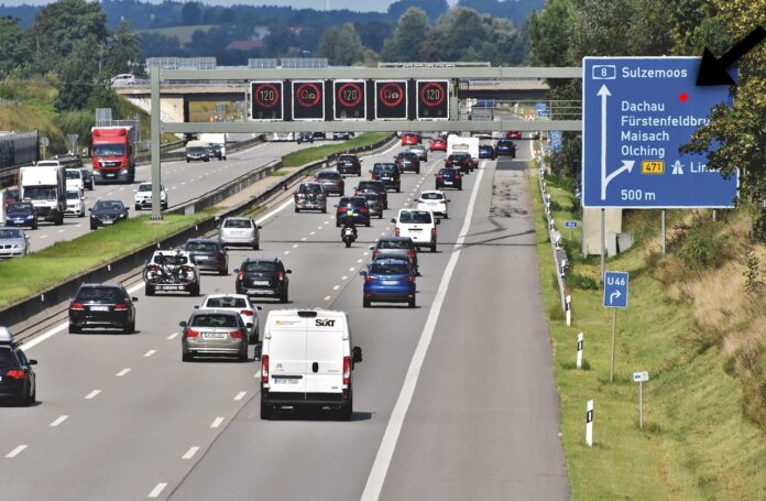Roter Punkt auf Verkehrsschild an einer Autobahn mit Autos und Autofahrer.