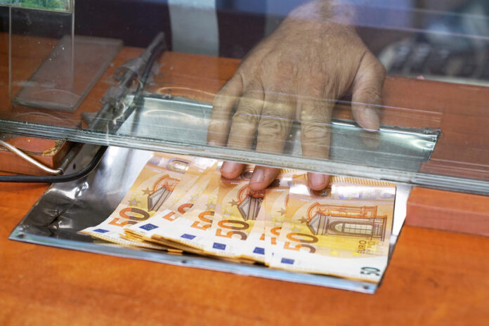 Eine Frau schiebt einige Fünfzig-Euro-Scheine durch einen Schlitz.