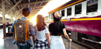 Ein Mann und zwei Frauen stehen auf einem Gleis, auf dem gerade ein Zug einfährt.
