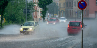 Mehrere Autos fahren über eine nasse Straße. Es regnet stark. Vorne sieht man ein Straßenschild.