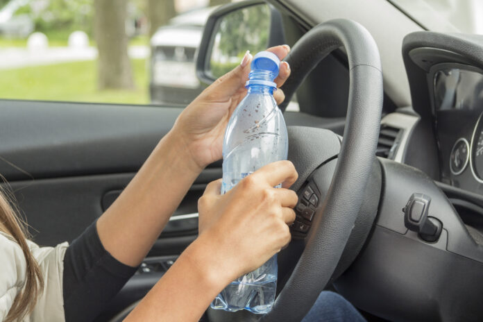 Autofahrerin hält Wasserflasche neben dem Lenkrad.