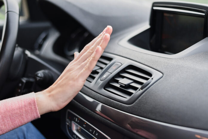 Eine Fahrerin hält ihre Hand vor die Klimaanlage in einem Fahrzeug