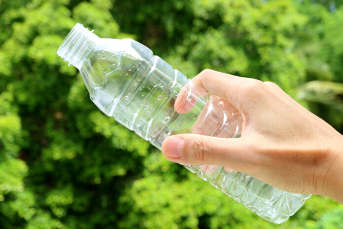 Im Garten hält eine Hand eine leere Plastikflasche.
