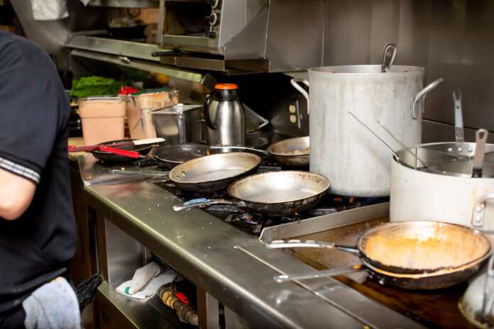 Eine stark beanspruchte Küche in einer Gaststätte mit schmutzigen Pfannen und Töpfen. Es kann sich um eine Küche in einem Restaurant oder in einem Café handeln. Der hygienische Standard ist mangelhaft. Eine Kontrolle würde dies beanstanden.